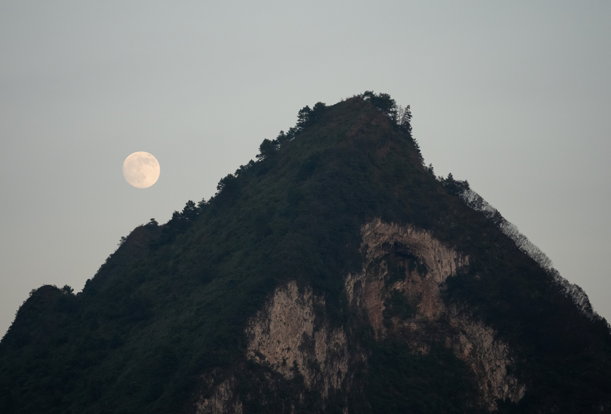 一轮淡月悬在青色山峰上方，暮色天空保持安静的留白。